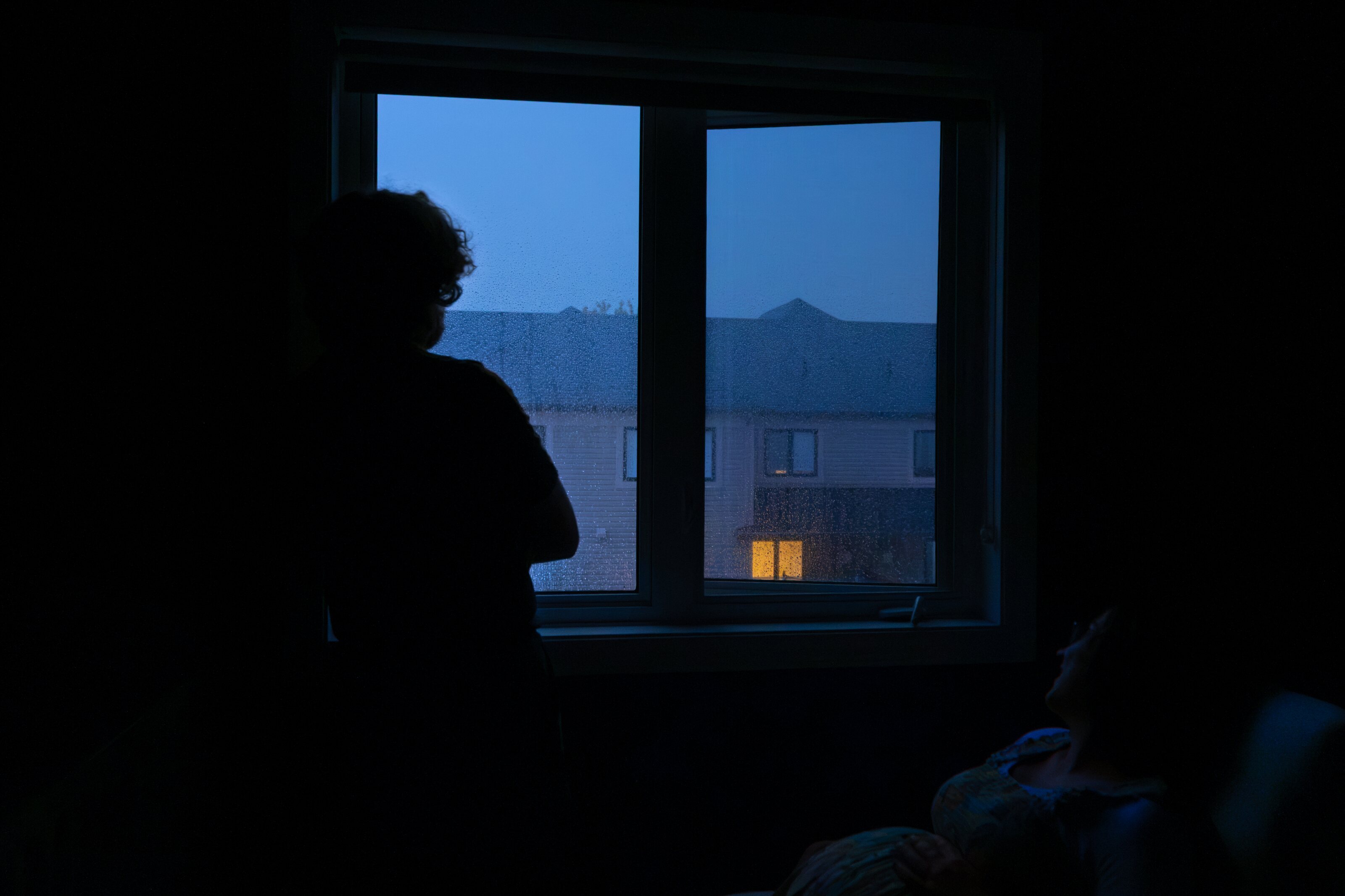 Figures silhouetted beside a rain-streaked window at dusk