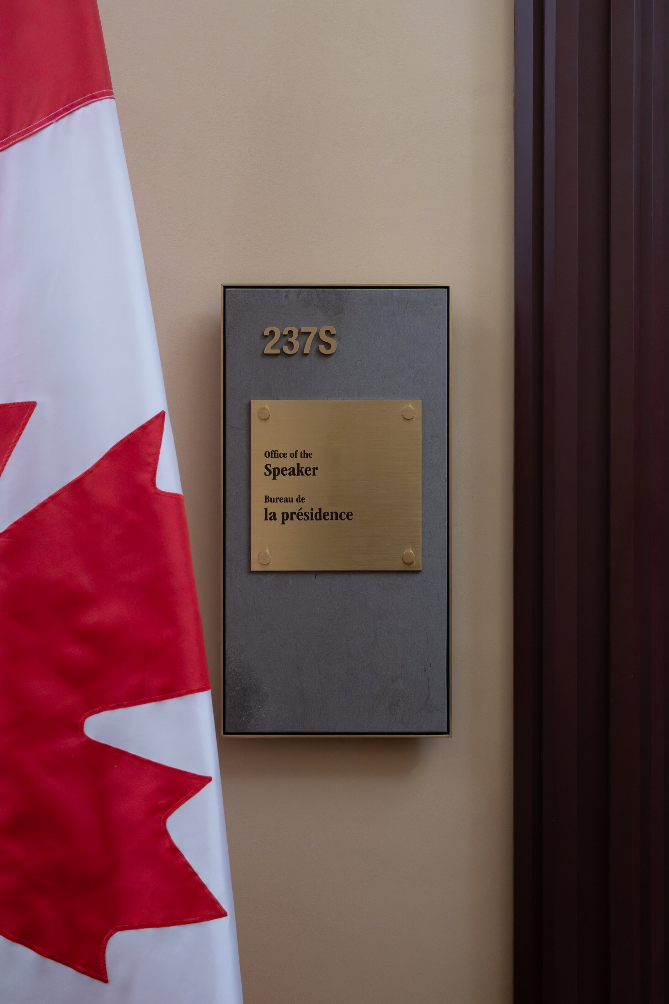 A Canadian flag beside a room plaque inside Parliament